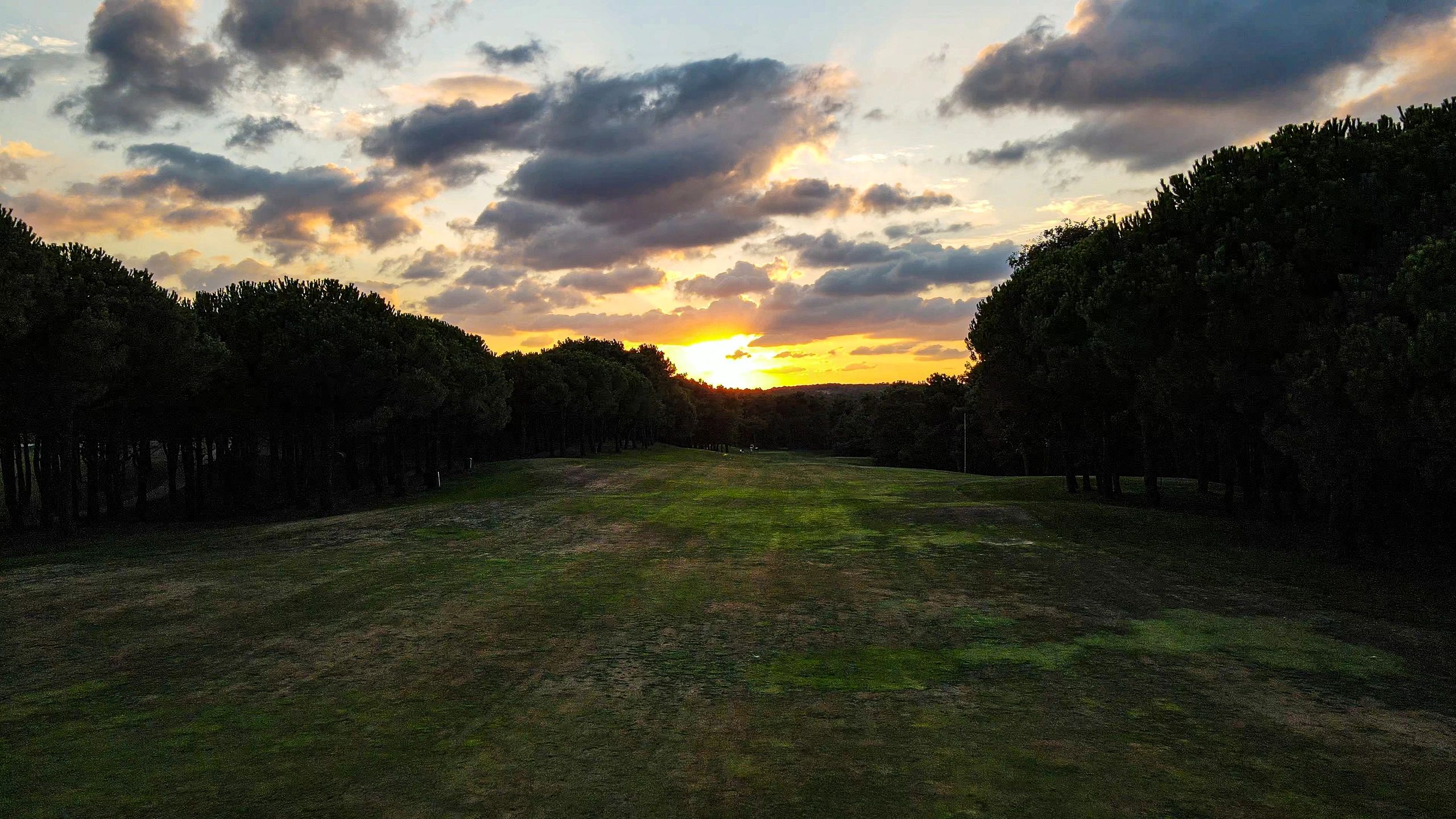 Vista aérea de un campo de golf tropical con fairways verdes y laguna al atardecer